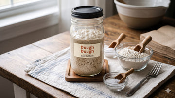 Beginner's sourdough starter setup - jar of starter, flour, water and a spoon on a wooden counter
